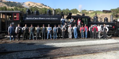 A large group of people most in railroad overalls standing in front of two steam locomotives