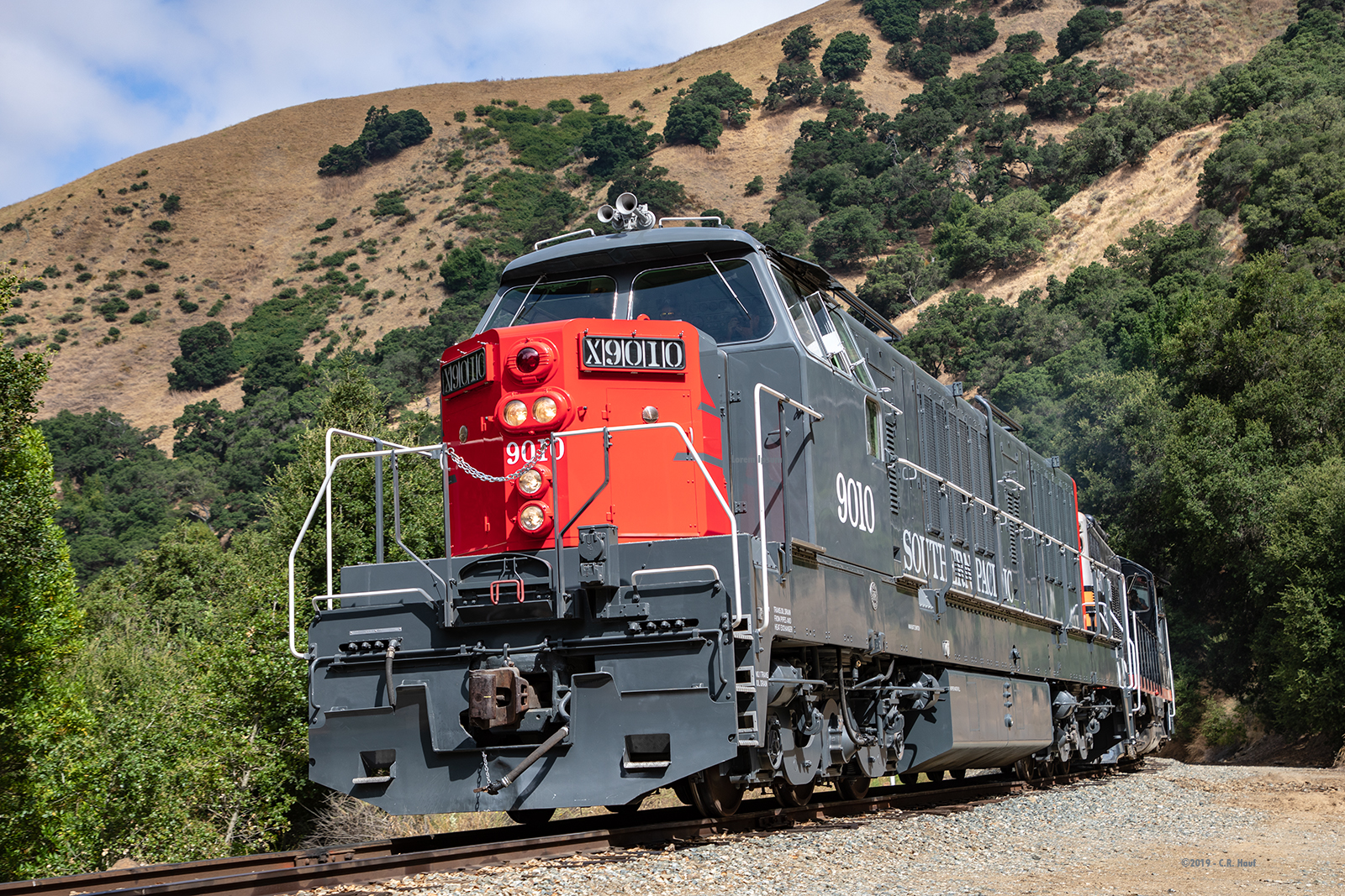 The very unique German-built diesel hydraulic locomotive once owned by the Southern Pacific Railroad and restored to that railroad's scarlet red and gray paint scheme rolls around a sweeping curve on the railroad.