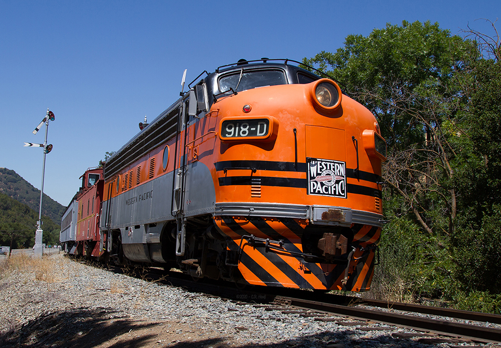 A classic cab style diesel locomotive in a bright orange, black and silver paint scheme of the Western Pacific Railroad leads the train along a curved section of railroad track.