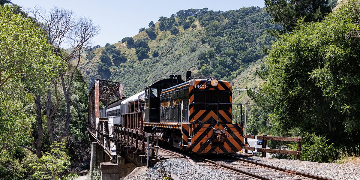 A historic diesel locomotive passes over a steel bridge in a canyon.
