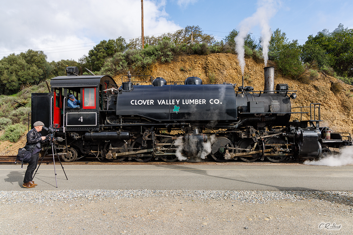 A side view of the museum's steam locomotive, Clover Valley Lumber Company #4, with a videographer standing next to the locomotive taking a video.