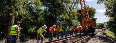 A group of men and women in work clothes line up along a newly installed piece of railroad track as they work to properly align the track.