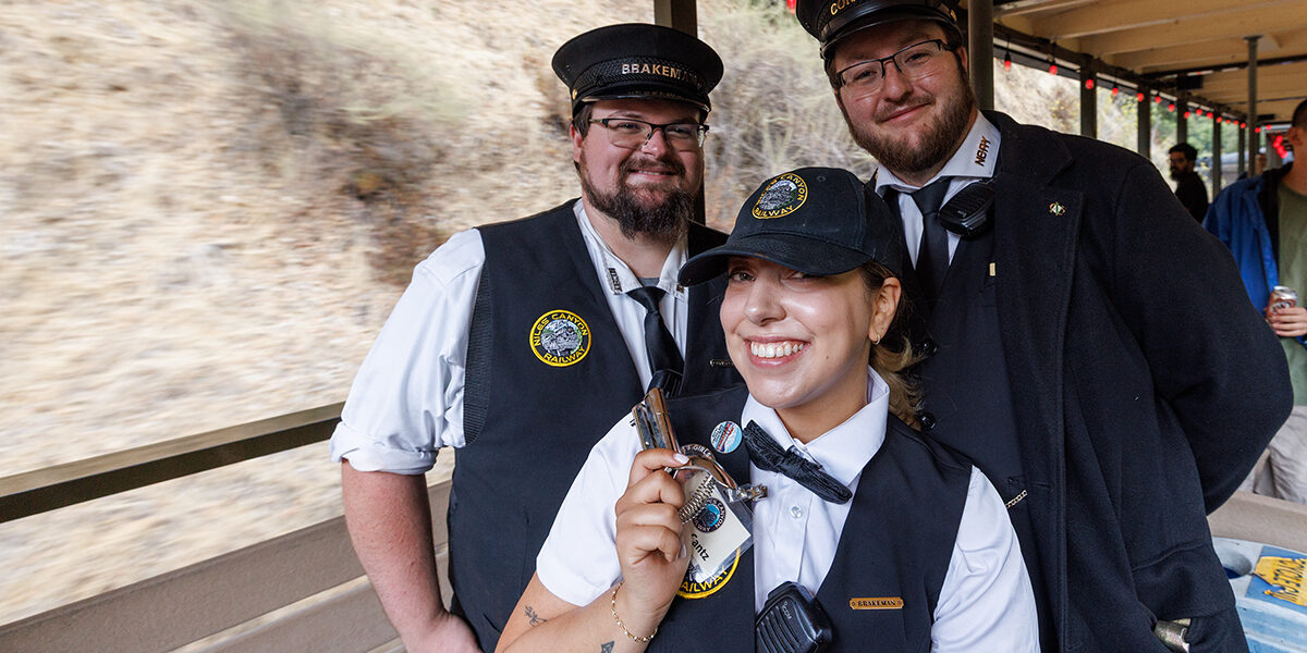 Two men and a woman in railroad conductors' uniforms who are part of the train crew pose in one of the railroad's open passenger cars.
